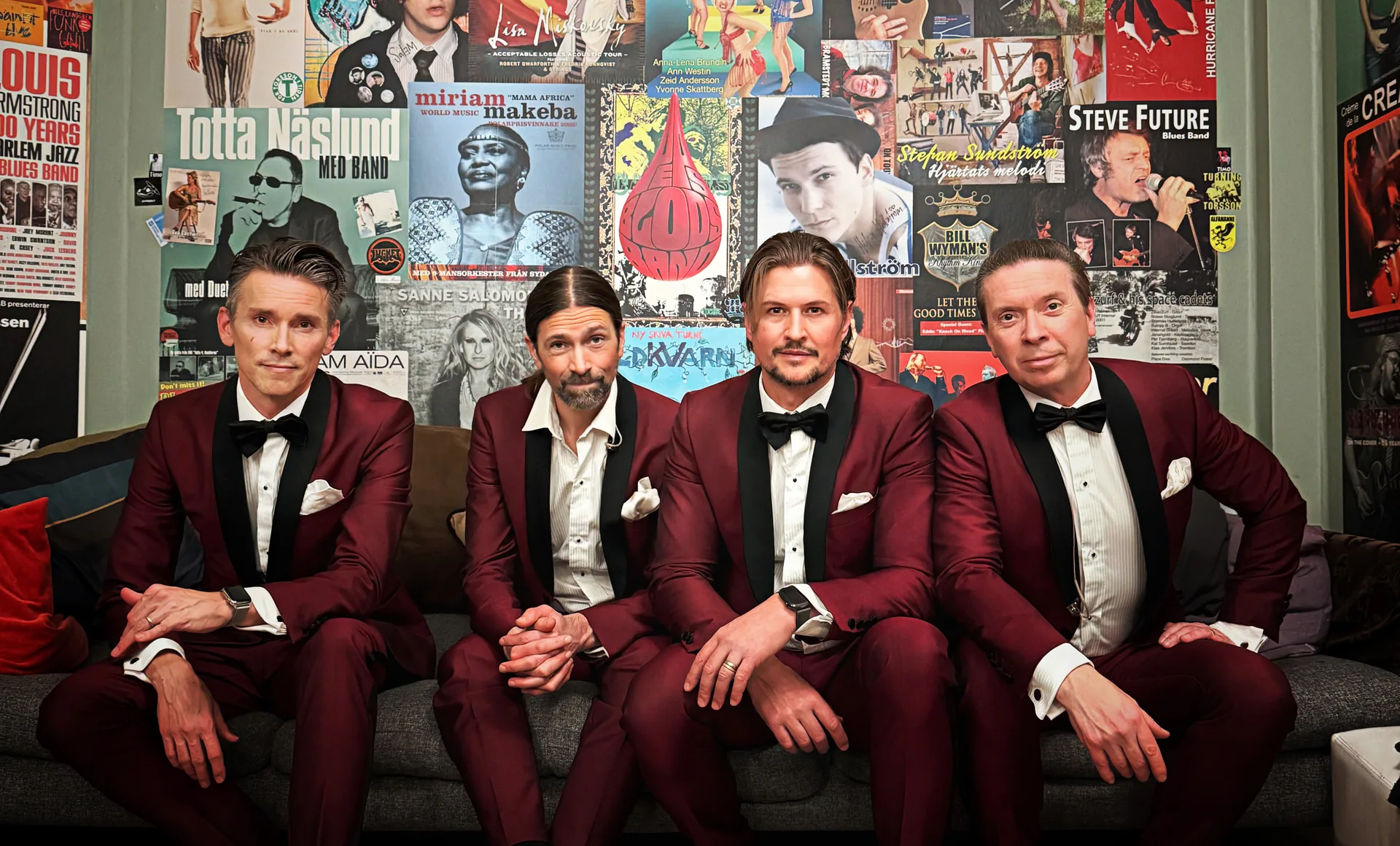 Niklas, Jonas, Henrik och Robert i vinröda smokingar i en soffa framför en vägg med musikaffischer